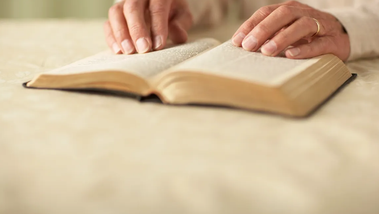 Hands reading an open Bible on a table