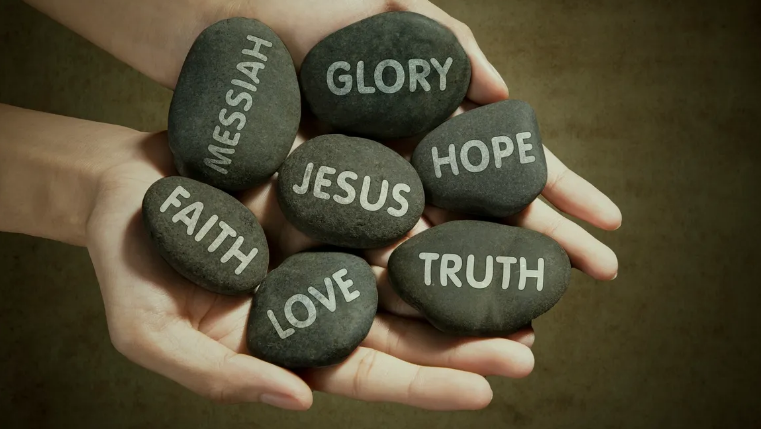 Hands holding stones with faith words: Messiah, Glory, Hope, Jesus, Faith, Love, Truth